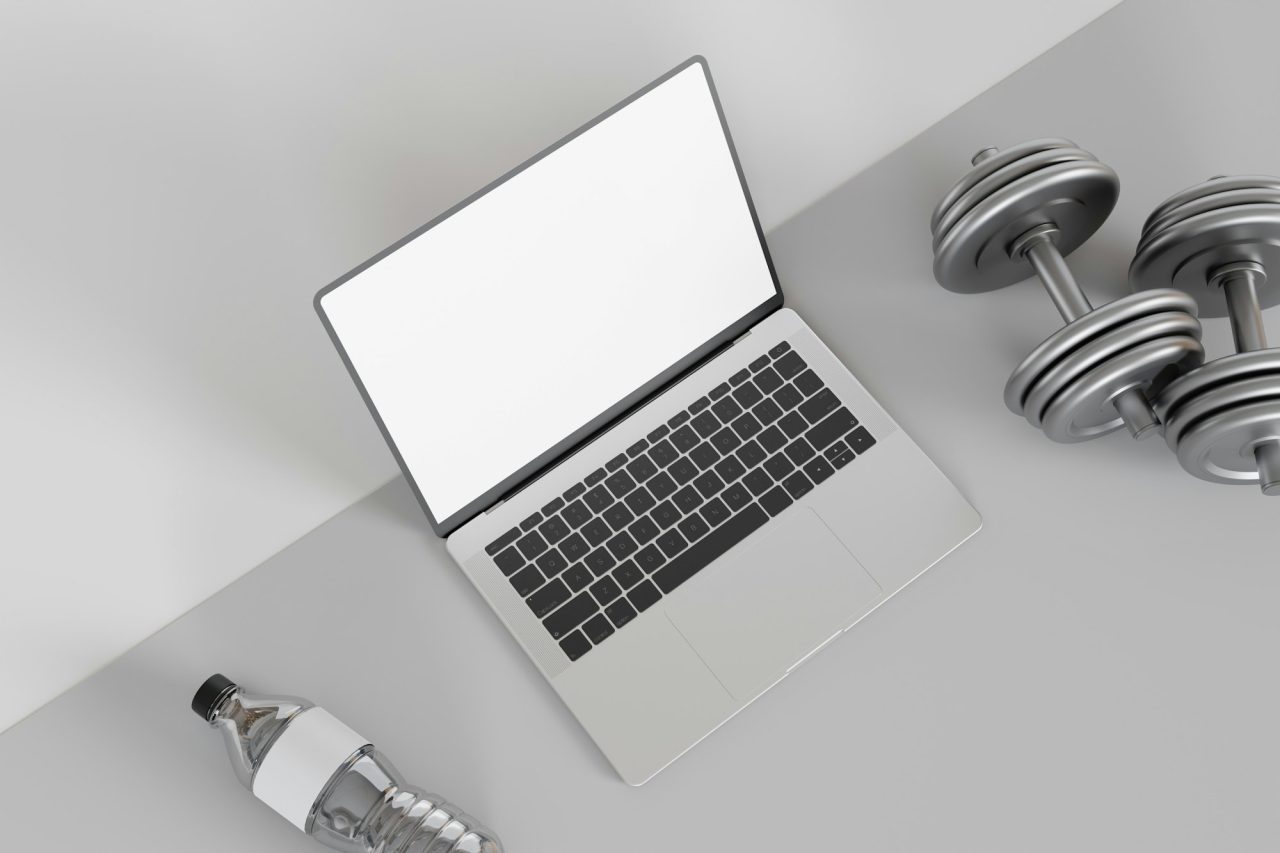 Laptop mockup with dumbbells and a water bottle on a fitness themed workspace